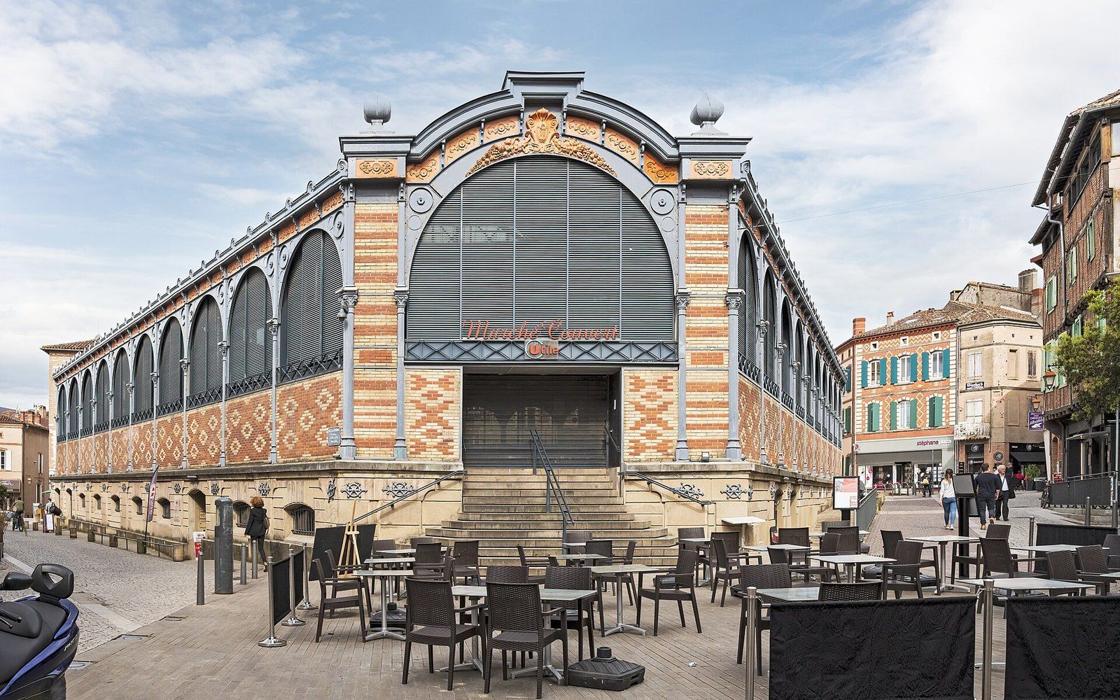 A covered market hall with produce stacked and adults shopping